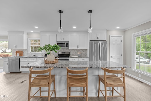 5804 Heathill Ct, Raleigh, NC 27603 - kitchen with appliances with stainless steel finishes, a center island, decorative backsplash, white cabinetry, and ornamental molding