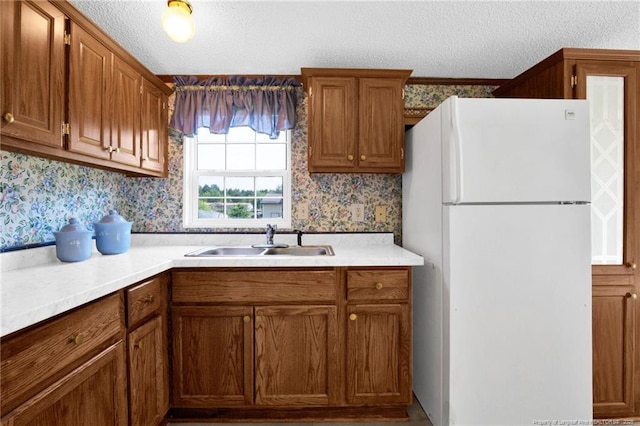 6131 Twiggs Ct, Hope Mills, NC 28348 - kitchen with freestanding refrigerator, wallpapered walls, a sink, a textured ceiling, and brown cabinets