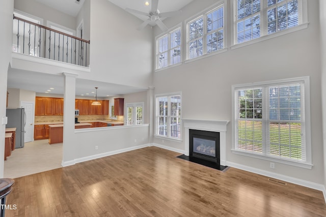 805 Alden Bridge Dr, Cary, NC 27519 - unfurnished living room featuring a high ceiling, a ceiling fan, light wood-type flooring, a fireplace with flush hearth, and baseboards