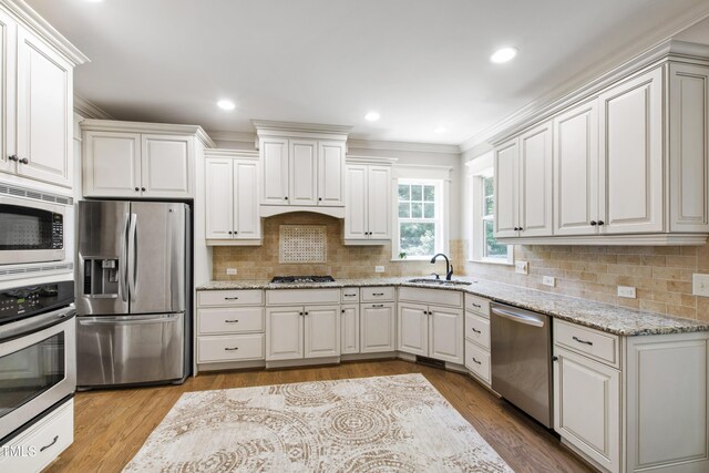 101 Eden Glen Dr, Holly Springs, NC 27540 - kitchen featuring appliances with stainless steel finishes, a sink, ornamental molding, decorative backsplash, and light stone countertops