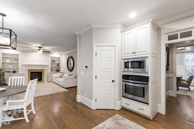 101 Eden Glen Dr, Holly Springs, NC 27540 - kitchen with stainless steel appliances, crown molding, a ceiling fan, white cabinetry, and a glass covered fireplace