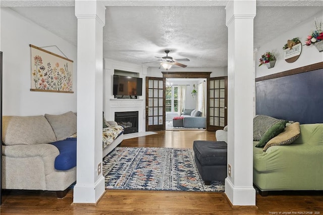 101 Quiet Cv, Raeford, NC 28376 - living room featuring ceiling fan, a fireplace with flush hearth, wood finished floors, ornate columns, and a textured ceiling
