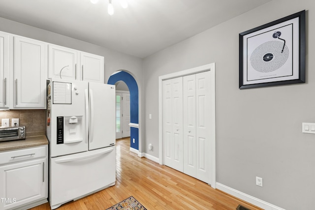 3821 La Costa Way, Raleigh, NC 27610 - kitchen with white refrigerator with ice dispenser, white cabinetry, light wood finished floors, baseboards, and backsplash