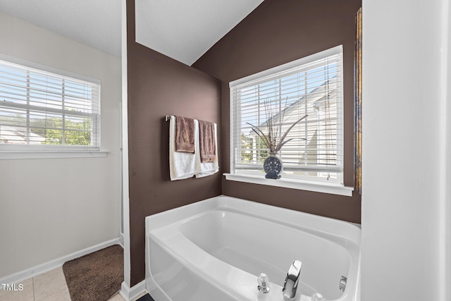 bathroom with a bath, vaulted ceiling, tile patterned floors, and baseboards
