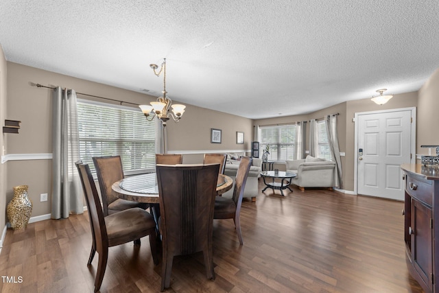 dining room with a textured ceiling, a chandelier, dark wood-type flooring, and baseboards