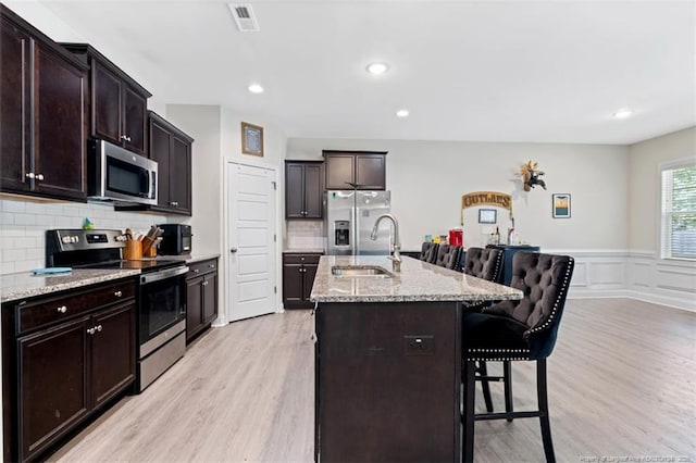 7680 Rufus Johnson Rd, Fayetteville, NC 28306 - kitchen featuring appliances with stainless steel finishes, light wood-style floors, a sink, a breakfast bar, and light stone countertops