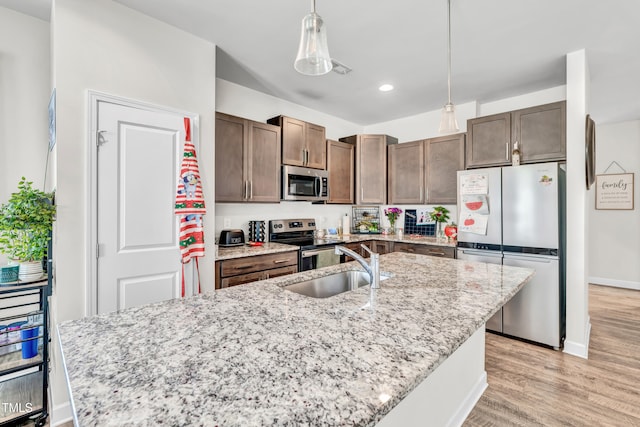 6760 Longitude Cir, Sims, NC 27880 - kitchen featuring appliances with stainless steel finishes, light wood finished floors, decorative light fixtures, light stone countertops, and a kitchen island with sink