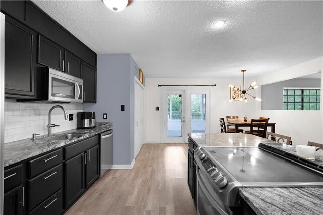 3855 Sturbridge Dr, Hope Mills, NC 28348 - kitchen with stainless steel appliances, a sink, a textured ceiling, dark cabinetry, and light wood-style floors