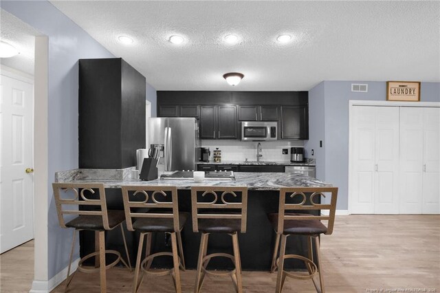 3855 Sturbridge Dr, Hope Mills, NC 28348 - kitchen with appliances with stainless steel finishes, a textured ceiling, backsplash, a breakfast bar area, and dark cabinets
