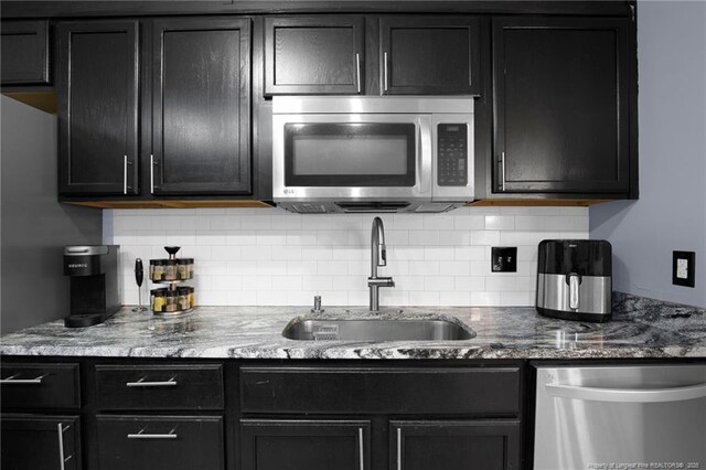 3855 Sturbridge Dr, Hope Mills, NC 28348 - kitchen with stainless steel appliances, a sink, dark cabinetry, decorative backsplash, and dark stone counters