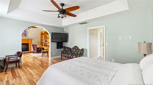 330 Wellington Rd, Saint Pauls, NC 28384 - bedroom with a tray ceiling, a glass covered fireplace, light wood finished floors, arched walkways, and a ceiling fan