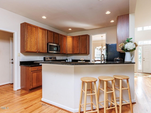 313 Hardwick Dr, Durham, NC 27713 - kitchen with stainless steel microwave, freestanding refrigerator, brown cabinetry, light wood-type flooring, and recessed lighting