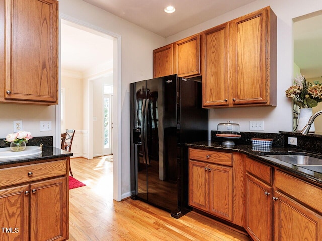 313 Hardwick Dr, Durham, NC 27713 - kitchen featuring black fridge with ice dispenser, light wood finished floors, brown cabinetry, recessed lighting, and dark stone countertops