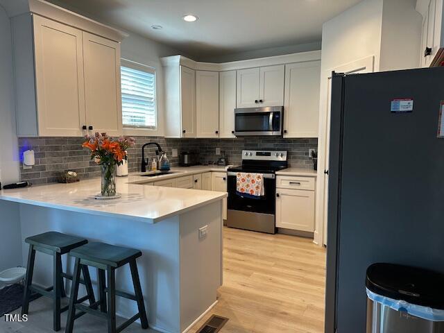 809 Trinity Park Dr, Wake Forest, NC 27587 - kitchen with appliances with stainless steel finishes, a peninsula, a sink, backsplash, and light wood-style flooring