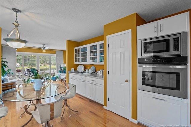 116 Fox Run Ct, West End, NC 27376 - kitchen with stainless steel appliances, a textured ceiling, light wood-style floors, white cabinetry, and glass insert cabinets