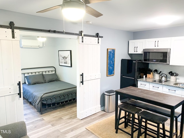 2907 University Dr, Durham, NC 27707 - bedroom featuring a barn door, freestanding refrigerator, a wall mounted air conditioner, light wood-type flooring, and ceiling fan
