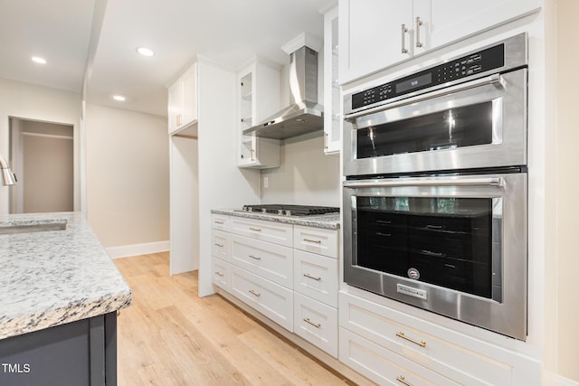 59 Cardinal Dr, Whispering Pines, NC 28327 - kitchen featuring appliances with stainless steel finishes, wall chimney exhaust hood, a sink, light wood-style flooring, and white cabinets