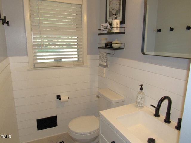 1700 Warrenton Rd, Henderson, NC 27537 - half bathroom featuring toilet, vanity, a wainscoted wall, and tile walls