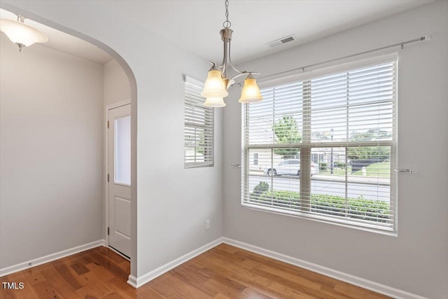 9327 Falkwood Rd, Raleigh, NC 27617 - empty room featuring arched walkways, a chandelier, wood finished floors, and baseboards
