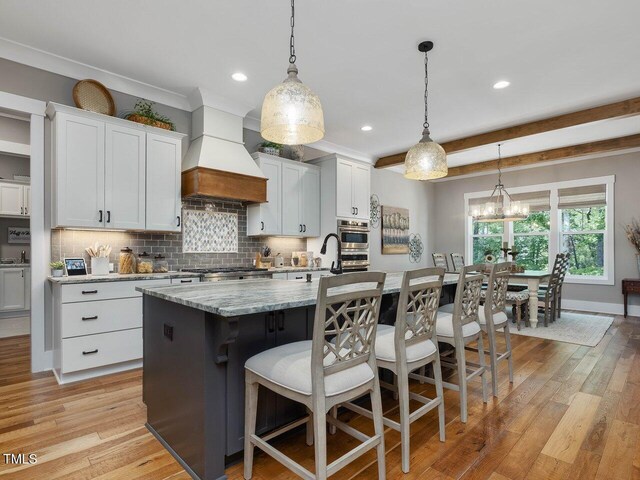 67 Spring Hollow Ct, Pittsboro, NC 27312 - kitchen featuring premium range hood, backsplash, a kitchen bar, a center island with sink, and stove