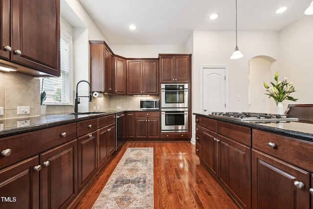7 Teahouse Ct, Durham, NC 27707 - kitchen with stainless steel appliances, a sink, dark wood-type flooring, arched walkways, and dark stone counters