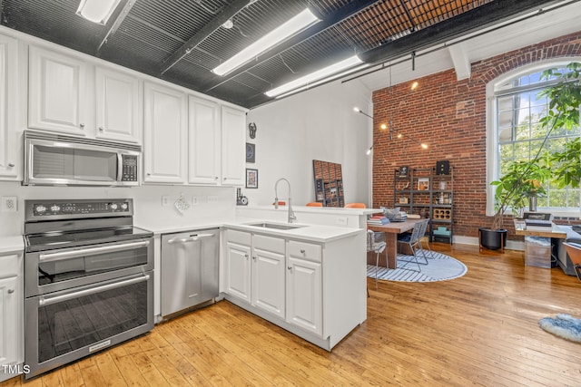 1535 Caraleigh Mills Ct Unit 210, Raleigh, NC 27603 - kitchen featuring appliances with stainless steel finishes, brick wall, a peninsula, light countertops, and light wood finished floors