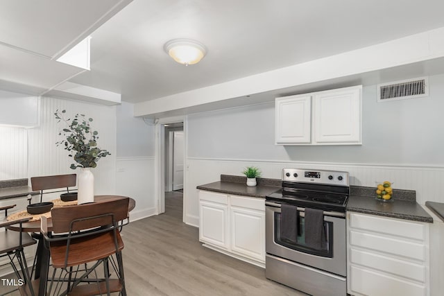 821 Onslow St, Durham, NC 27705 - kitchen with electric stove, dark countertops, white cabinets, light wood-style floors, and a wainscoted wall
