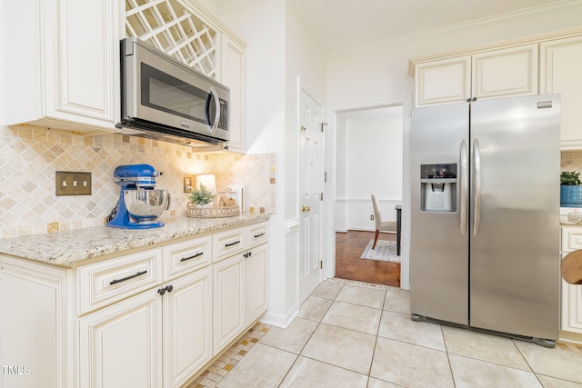 8913 Walking Stick Trl, Raleigh, NC 27615 - kitchen featuring appliances with stainless steel finishes, cream cabinetry, ornamental molding, backsplash, and light stone countertops