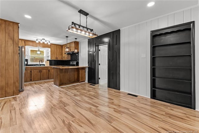 3902 Hartwell Rd, Fayetteville, NC 28304 - kitchen featuring freestanding refrigerator, brown cabinetry, light wood finished floors, under cabinet range hood, and decorative light fixtures