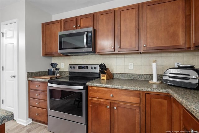 625 Fairfield Cir, Raeford, NC 28376 - kitchen with appliances with stainless steel finishes, dark countertops, light wood finished floors, backsplash, and brown cabinets