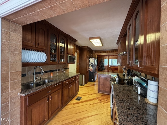 603 Hugo St, Durham, NC 27704 - kitchen with stainless steel microwave, a sink, light wood-type flooring, glass insert cabinets, and dark stone counters