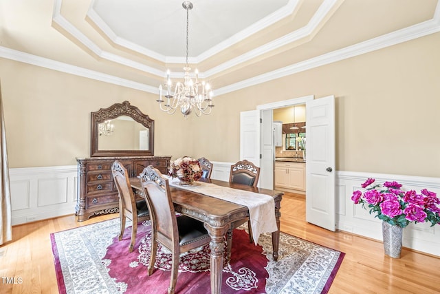 1317 Woodgate Manor Ct, Raleigh, NC 27614 - dining space featuring a chandelier, a raised ceiling, crown molding, light wood finished floors, and a wainscoted wall