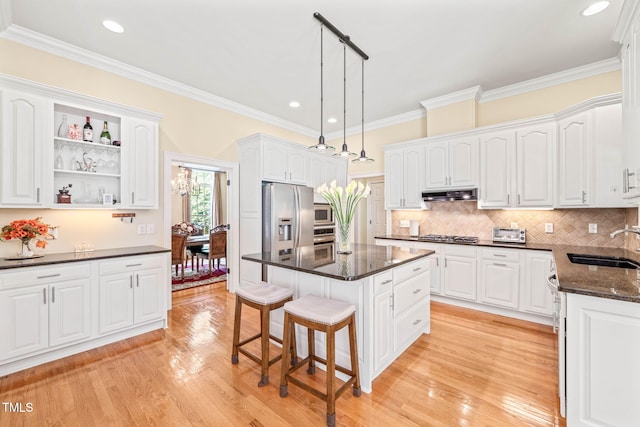 1317 Woodgate Manor Ct, Raleigh, NC 27614 - kitchen featuring appliances with stainless steel finishes, under cabinet range hood, a kitchen breakfast bar, light wood finished floors, and ornamental molding