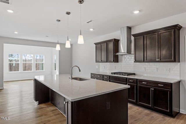 219 Berry Mill Ln Unit 179, Raleigh, NC 27603 - kitchen with wall chimney exhaust hood, a sink, stainless steel gas stovetop, decorative backsplash, and light wood-type flooring