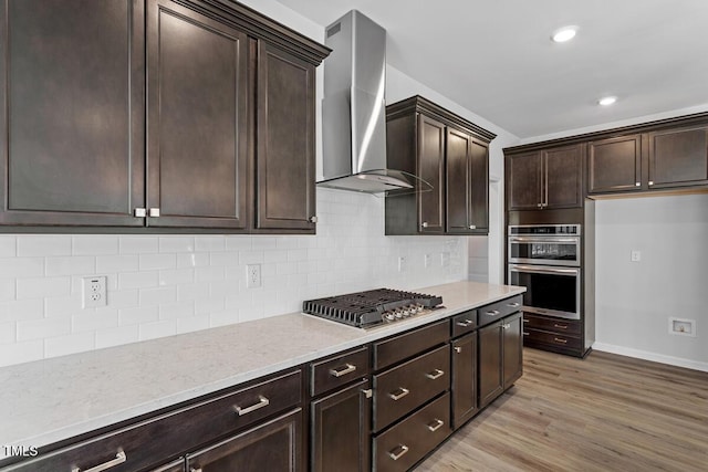 219 Berry Mill Ln Unit 179, Raleigh, NC 27603 - kitchen featuring wall chimney exhaust hood, appliances with stainless steel finishes, dark brown cabinets, light wood finished floors, and baseboards