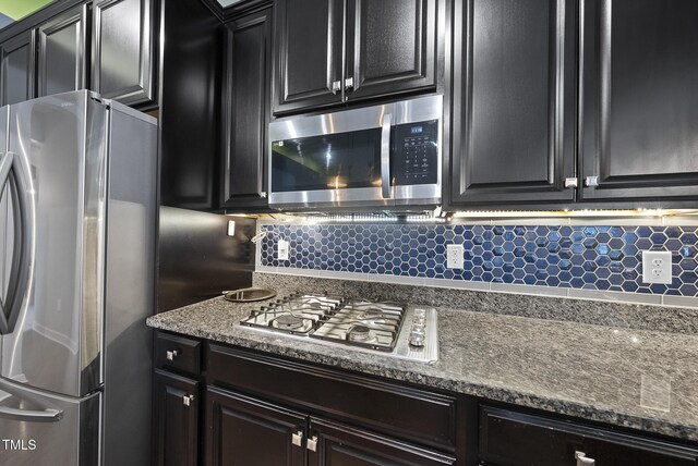 2909 Landon Pines Ct, New Hill, NC 27562 - kitchen with appliances with stainless steel finishes, backsplash, dark cabinetry, and dark stone counters