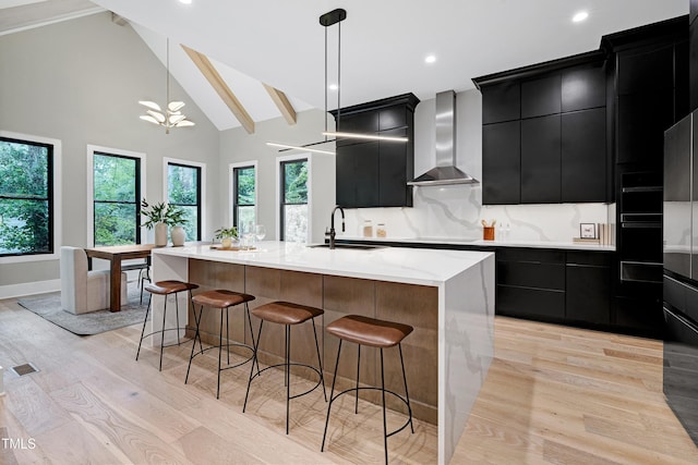 5406 Garrett Rd, Durham, NC 27707 - kitchen with dark cabinets, wall chimney range hood, light wood-type flooring, a breakfast bar, and hanging light fixtures