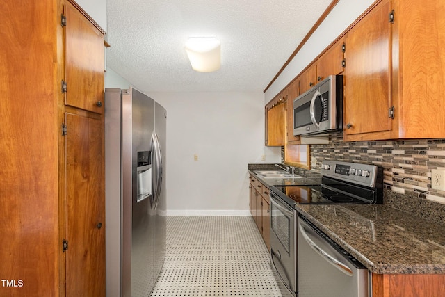 1304 Park Ave, Dunn, NC 28334 - kitchen with appliances with stainless steel finishes, baseboards, a textured ceiling, brown cabinetry, and tasteful backsplash