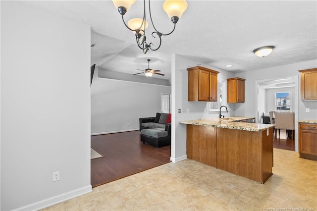 1517 Seabiscuit Dr, Parkton, NC 28371 - kitchen with a ceiling fan, brown cabinetry, a peninsula, open floor plan, and light stone countertops