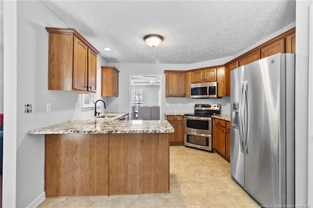 1517 Seabiscuit Dr, Parkton, NC 28371 - kitchen with appliances with stainless steel finishes, a peninsula, a sink, brown cabinetry, and a textured ceiling