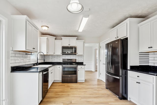 128 Newton Ct, Raeford, NC 28376 - kitchen featuring stainless steel appliances, a sink, dark countertops, light wood-style flooring, and white cabinets