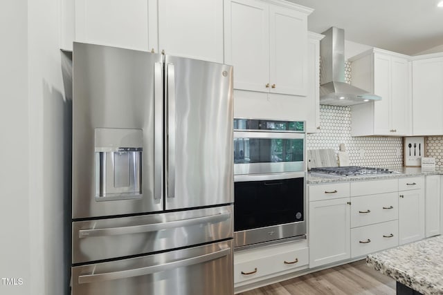 187 Harpers Landing Rd, Garner, NC 27529 - kitchen with appliances with stainless steel finishes, wall chimney range hood, light wood-style flooring, white cabinetry, and backsplash