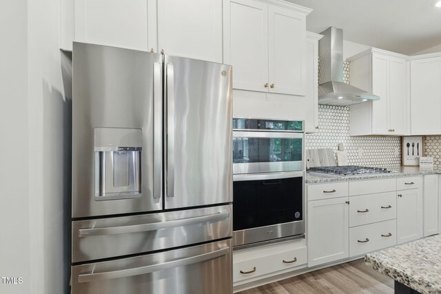 187 Harpers Landing Rd, Garner, NC 27529 - kitchen with appliances with stainless steel finishes, wall chimney range hood, light wood-style flooring, white cabinetry, and backsplash
