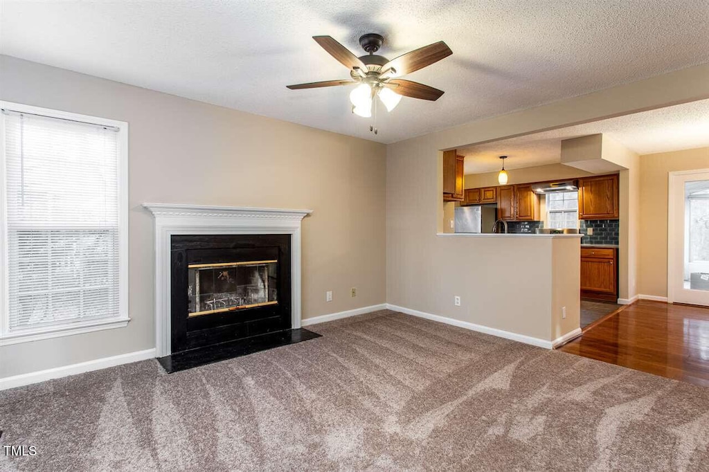 4009 Olde Coach Rd, Durham, NC 27707 - unfurnished living room featuring dark colored carpet, a ceiling fan, baseboards, a fireplace with flush hearth, and a textured ceiling