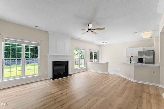 107 Woolard Way, Apex, NC 27502 - unfurnished living room with a ceiling fan, light wood-type flooring, a textured ceiling, a sink, and a fireplace