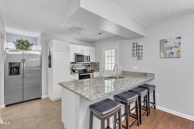 8361 Mcguire Dr, Raleigh, NC 27616 - kitchen featuring appliances with stainless steel finishes, a textured ceiling, a peninsula, a breakfast bar area, and white cabinets