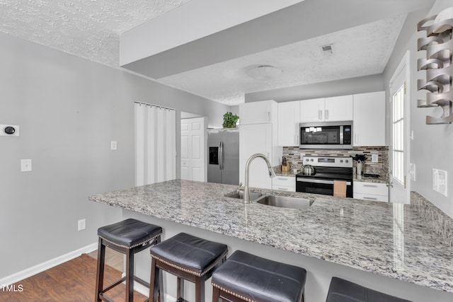 8361 Mcguire Dr, Raleigh, NC 27616 - kitchen featuring appliances with stainless steel finishes, a textured ceiling, light stone countertops, dark wood-type flooring, and a peninsula