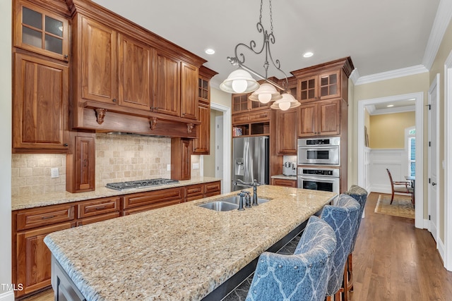 105 Somerley Dr, Garner, NC 27529 - kitchen featuring stainless steel appliances, a sink, brown cabinetry, ornamental molding, and a wainscoted wall