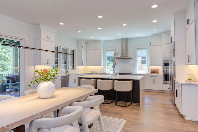 2114 Cowper Dr, Raleigh, NC 27608 - kitchen featuring wall chimney range hood, dishwasher, recessed lighting, light wood-style flooring, and white cabinetry