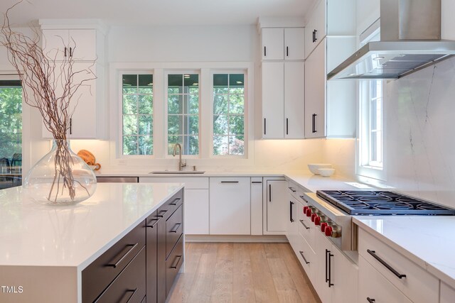2114 Cowper Dr, Raleigh, NC 27608 - kitchen featuring wall chimney range hood, stainless steel gas stovetop, light wood-type flooring, white cabinets, and decorative backsplash